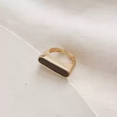 Anel dourado ajustável com design liso e detalhe resinado na cor preta, em banho hipoalergênico de ouro 18k.