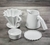 Kit de Jarra e Coador de Café 102 em Cerâmica com esmaltação branca da Felline Cerâmica. Vista de 4 peças deste conjunto sobre uma mesa de madeira, coador, jarra, prato de apoio e corta pingos. 